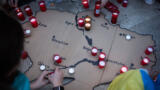 Eine Ukrainekarte aus Pappe mit darauf platzierten Kerzen. Menschen knien um die Karte herum.