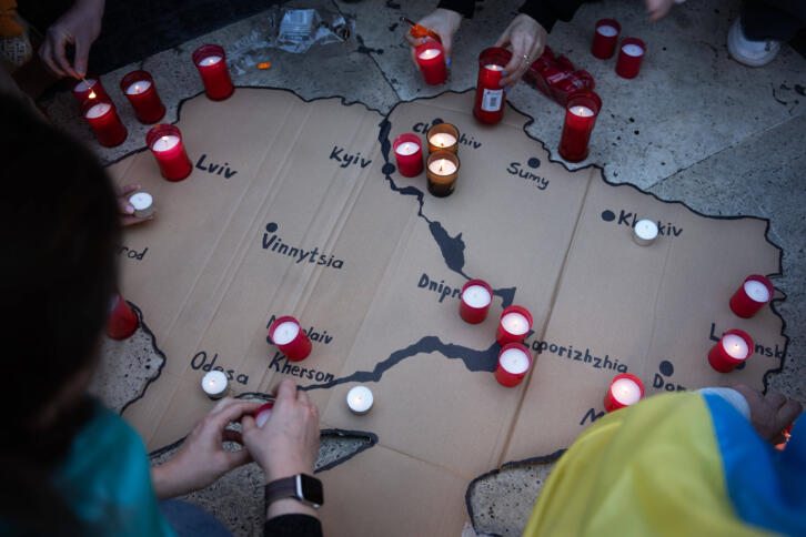 Eine Ukrainekarte aus Pappe mit darauf platzierten Kerzen. Menschen knien um die Karte herum.