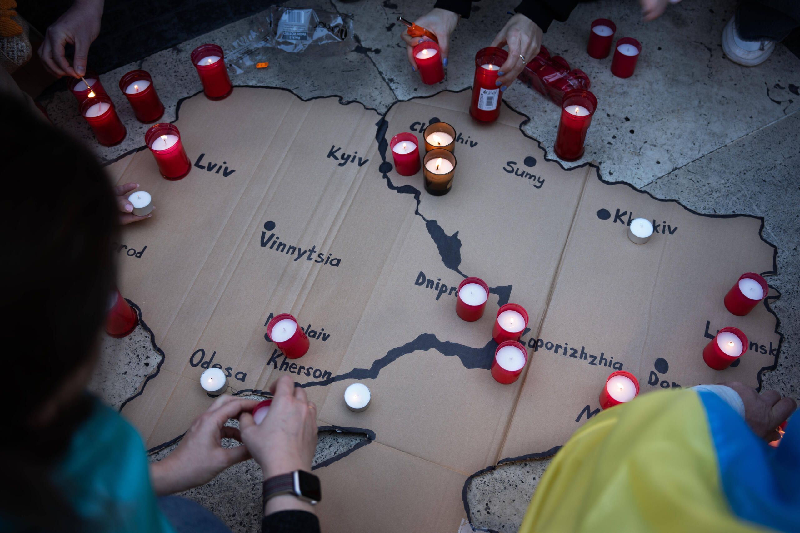 Eine Ukrainekarte aus Pappe mit darauf platzierten Kerzen. Menschen knien um die Karte herum.