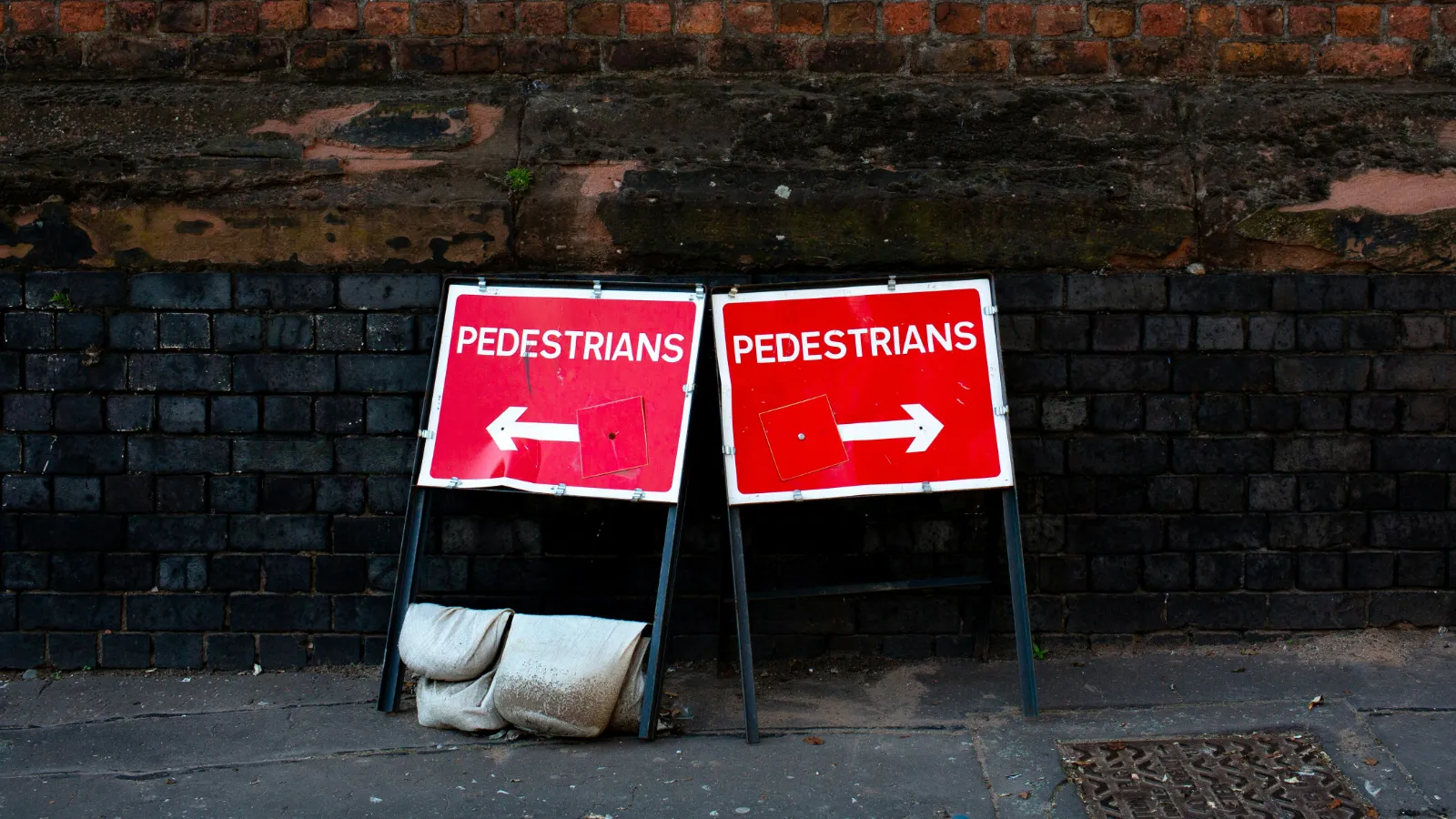 Zwei rote Wegweiser vor einer Ziegelwand, die in verschiedene Richtungen weisen