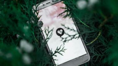 Ein Handy liegt auf einem grünen Pflanzenuntergrund, das Display zeigt ein Herz in einer Sprechblase