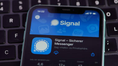 Handy auf dem ein Signal-Logo zu sehen ist, dahinter eine Tastatur