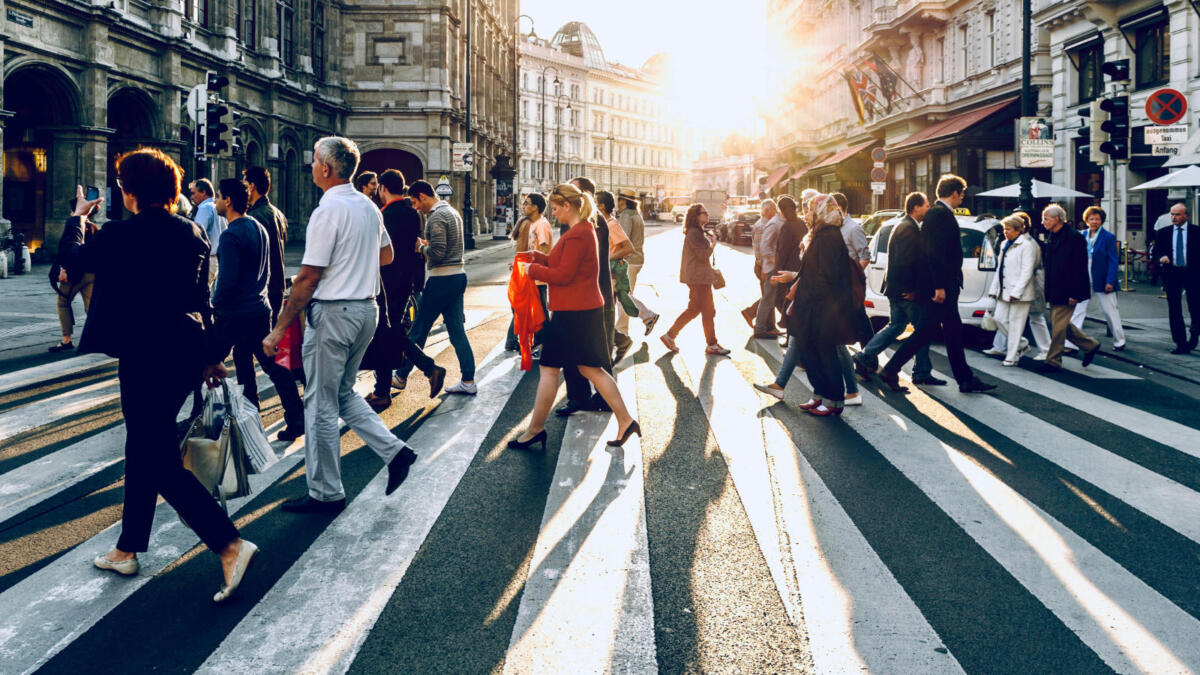 Menschen gehen vor untergehender Sonne über einen Zebrastreifen
