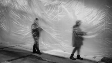 Auf dem schwarz-weißen Bild sind zwei Menschen zu sehen, die sich ihren Weg entlang einer halbdurchsichtigen Folie bahnen.