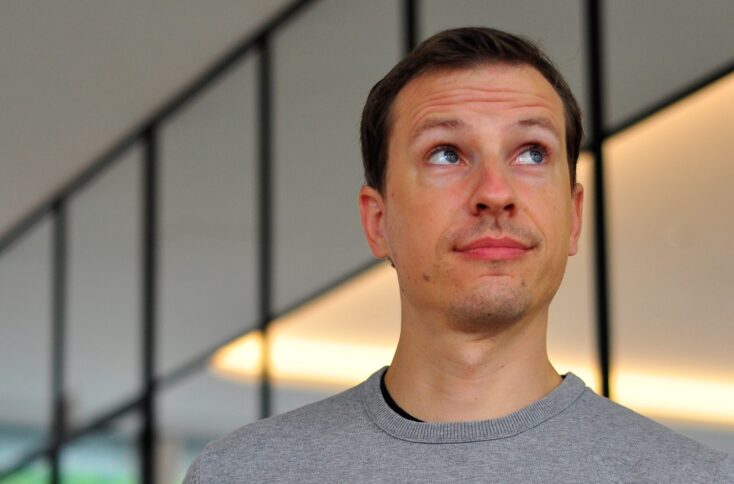 Ein Mann mit kurzen Haaren in einem grauen T-Shirt schaut zur Seite.