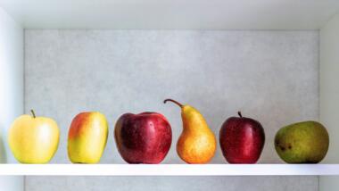 Auf einem Regalbrett liegen fünf Äpfel und eine Birne
