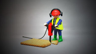 Playmobilmännchen mit Presslufthammer hämmert auf einem Keks