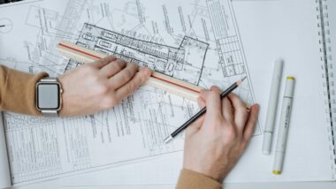 Männliche Hände halten ein Lineal auf einen fein gezeichneten Bauplan.