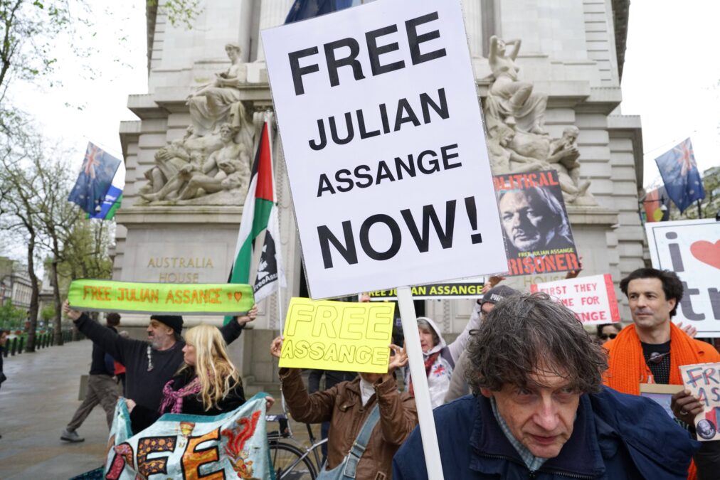 Menschen mit Protestschildern, auf einem steht "Free Julian Assange Now"