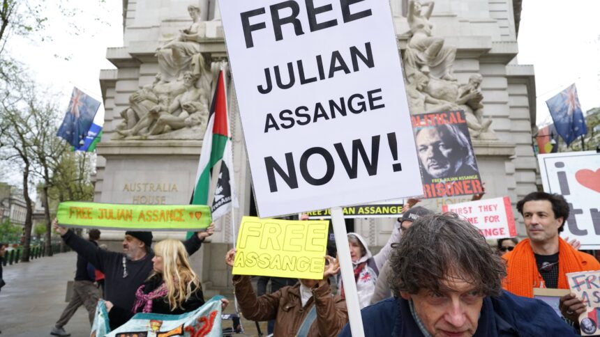 Menschen mit Protestschildern, auf einem steht "Free Julian Assange Now"