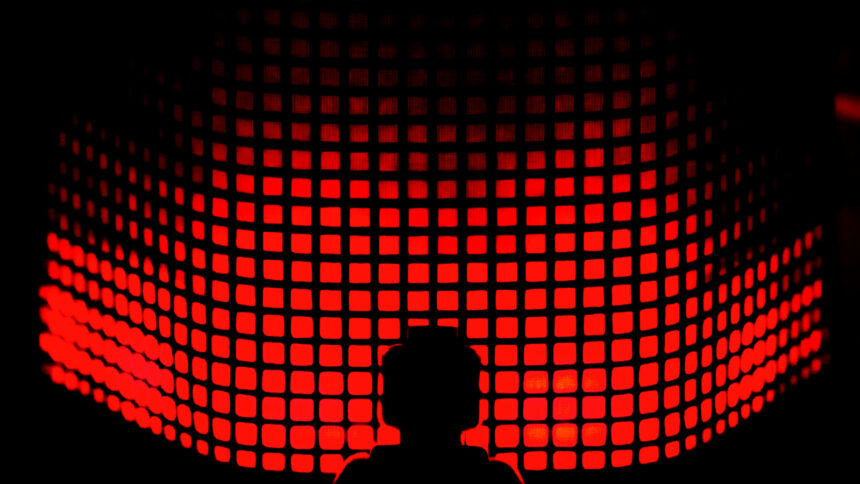 A wall of glowing red rectangles, in front of it the shadow of a person