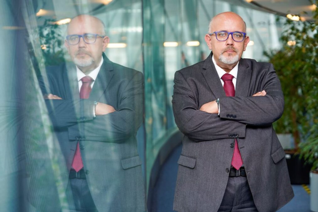 Wiewiórowski steht neben einer Glaswand, in der er sich spiegelt.