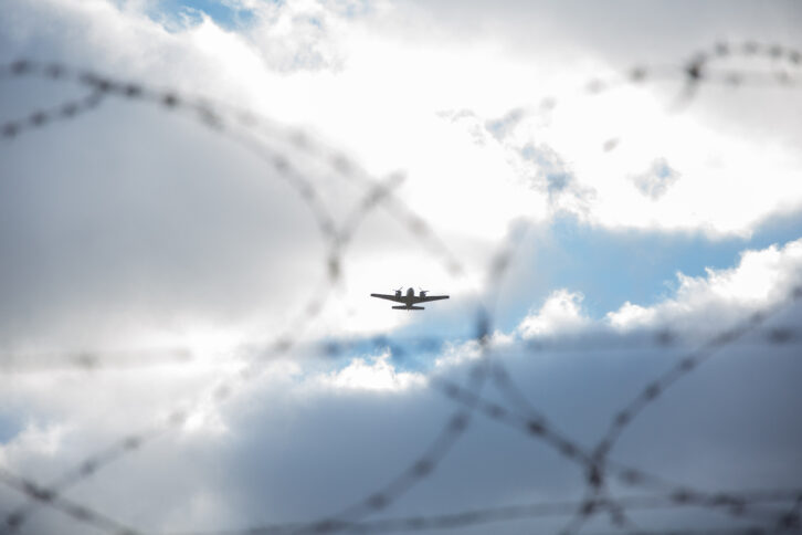 Die Silhouette eines zweimotorigen Flugzeuges hinter Stacheldraht.