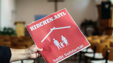 Schild mit der Aufschrift "Kirchenasyl heisst Solidaritaet" in einer evangelischen Kirche, im Hintergrund ein Kreuz