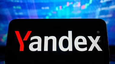 Ein Smartphone vor blau schimmerndem Hintergrund, darauf das Logo des Yandex-Konzerns