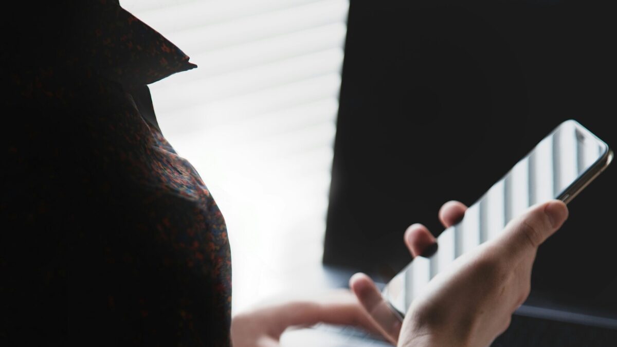 Fotoaufnahme, die einem Menschen über die Schulter auf ein Smartphone schaut, dessen Display in der Sonne reflektiert.