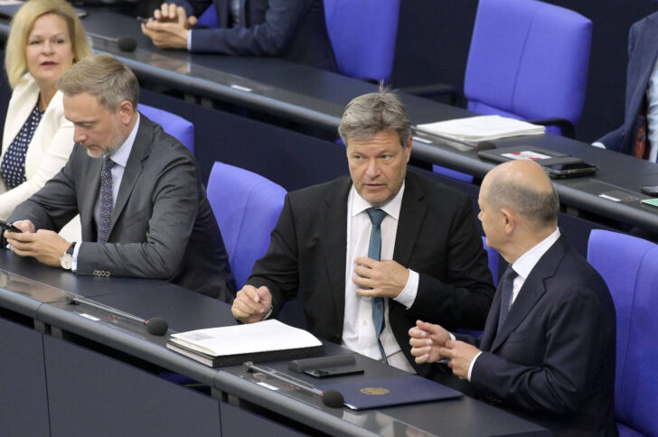 Eine Frau im hellen Blazer und drei Männer in dunklen Anzügen