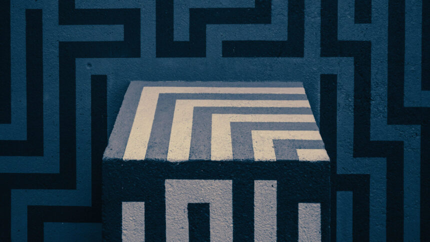 Ein Würfel mit einem labyrinth-ähnlichen Muster vor einer Wand mit einer ähnlichen Bemalung