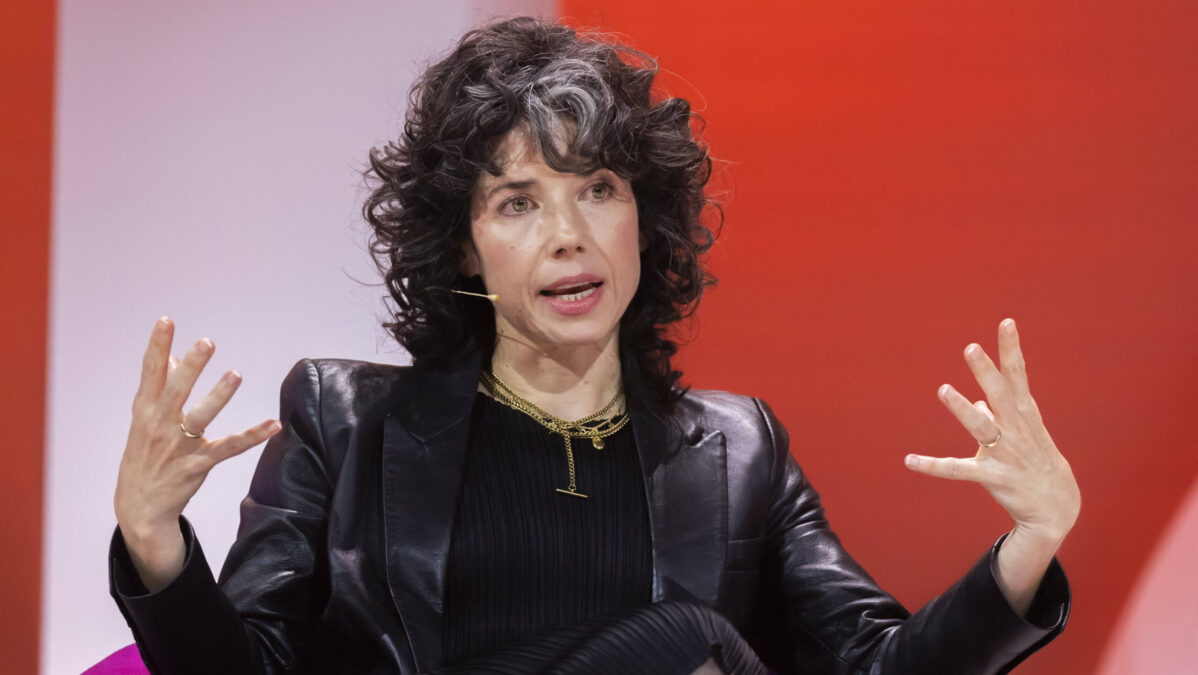 Sitzende Frau erhebt beide Hände in einer Geste.