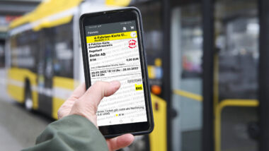 Ein Smartphone mit einem digitalen BVG-Ticket, dahinter ein wartender Bus.