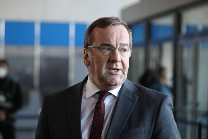 Person mit Brille, dunklem Anzug und Krawatte vor einer Glastür