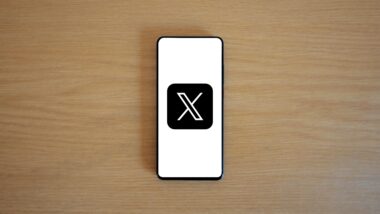 Ein Handy liegt auf einem Holztisch. Es zeigt das Logo von X, früher Twitter.