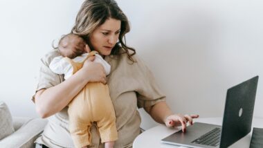 Eine junge Mutter hält ein aby auf dem Arm, während sie einen Laptop benutzt.