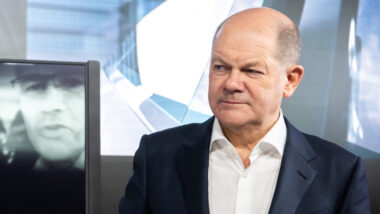 Olaf scholz betrachtet mit skeptischem Gesichtsausdruck ein halb-transparentes Display