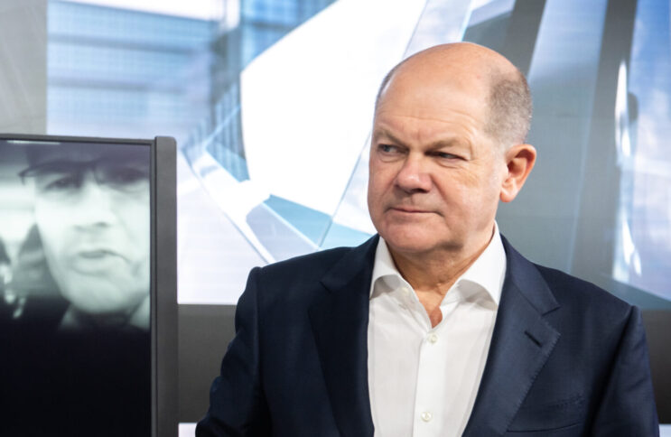 Olaf scholz betrachtet mit skeptischem Gesichtsausdruck ein halb-transparentes Display