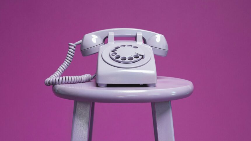 Ein Wählscheiben-Telefon steht auf einem Hocker vor lila Hintergrund