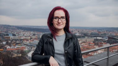 Markéta Gregorová standing at a guardrail with a view of a city behind her.