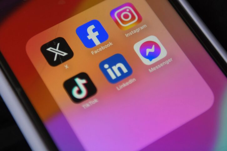 Smartphone-Bildschirm zeigt Icons von Facebook, X, Insta und TikTok.