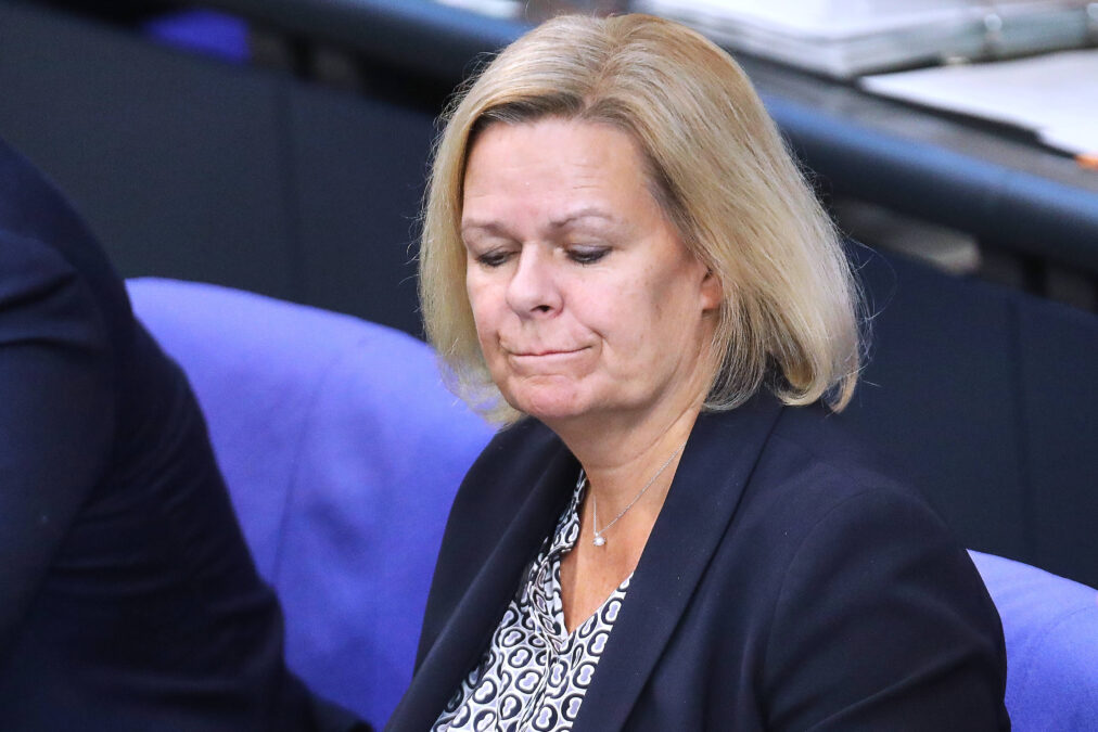 Bild einer blonden Frau mit schwarzem Blazer, die sich auf die Lippen beißt.