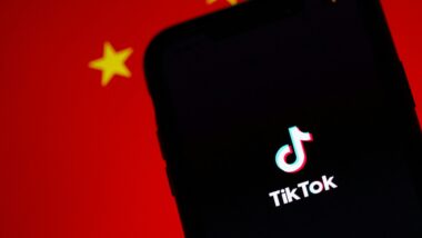 Ein dunkles Handy mit TikTok-Logo vor einer verschwommenen China Flagge.