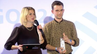 Frau mit Mikrofon, Mann mit Preis (eine Art Pokal) in der Hand