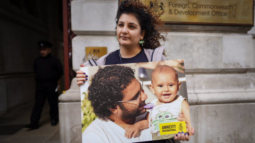 Eine Frau hält ein Demoschild, darauf Alaa mit einem kleinen Kind auf dem Arm und das Logo von Amnesty International.