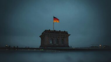 Düsteres Bild eines massiven Eckturmes des Reichtstagsgeböudes mit einer Deutschlandflagge und einer dunklen, wolkenverhangenen Himmel