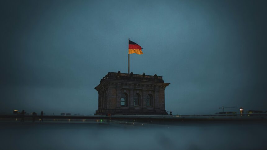 Düsteres Bild eines massiven Eckturmes des Reichtstagsgeböudes mit einer Deutschlandflagge und einer dunklen, wolkenverhangenen Himmel