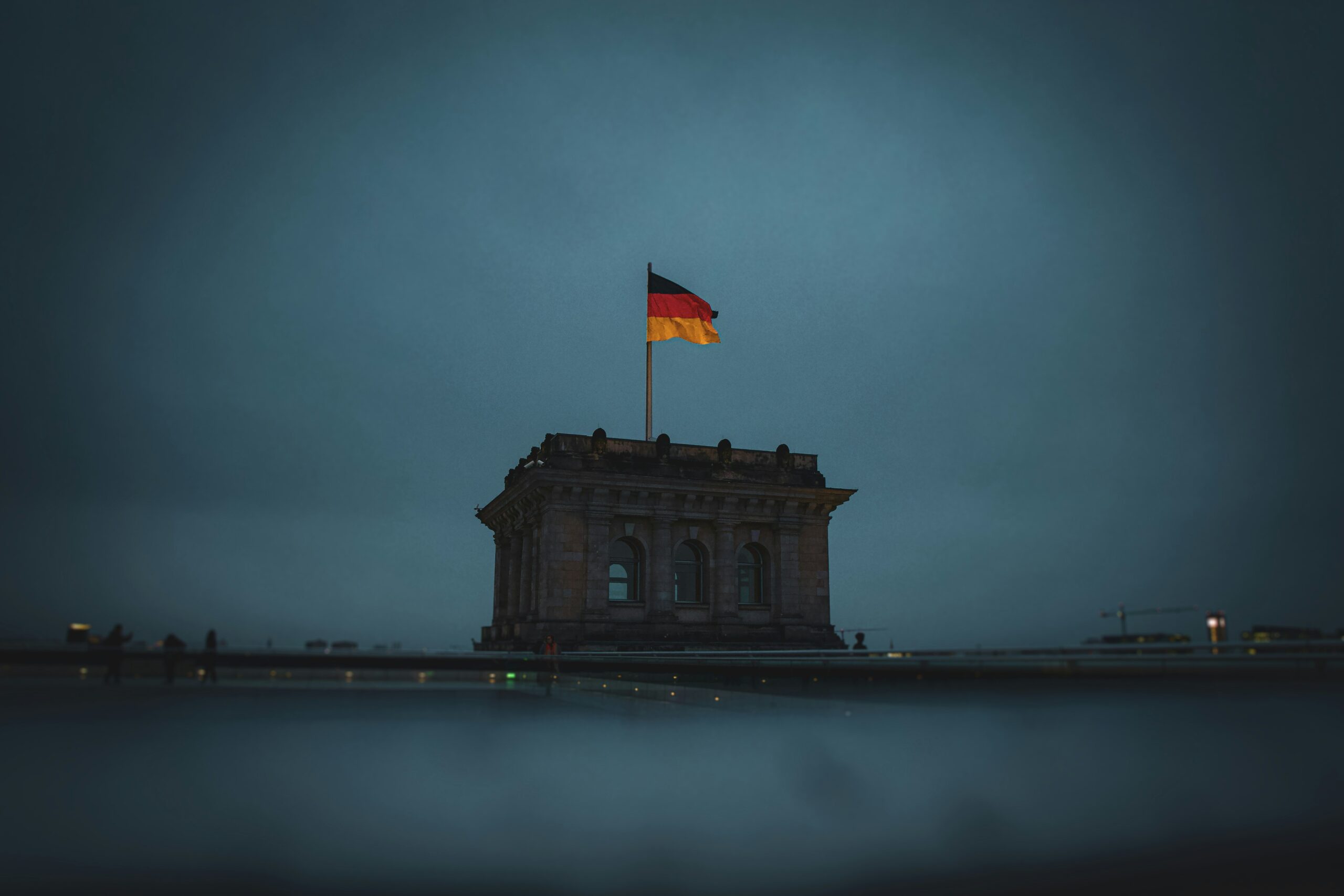Düsteres Bild eines massiven Eckturmes des Reichtstagsgeböudes mit einer Deutschlandflagge und einer dunklen, wolkenverhangenen Himmel