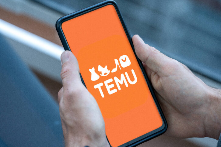 Ein Handy zeigt den Startbildschirm der Temu-App. Zwei Männerhände halten das Handy.