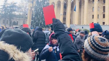 Mann hält eine rote Karte vor dem georgischen Parlament hoch.