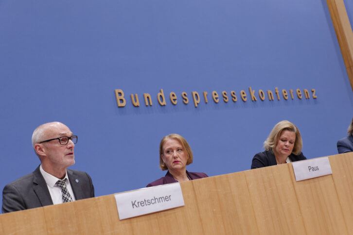 Drei Personen vor einer blauen Wand, dahinter Schriftzug "Bundespressekonferenz"