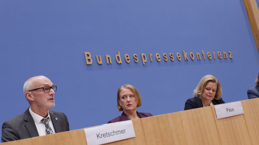 Drei Personen vor einer blauen Wand, dahinter Schriftzug "Bundespressekonferenz"