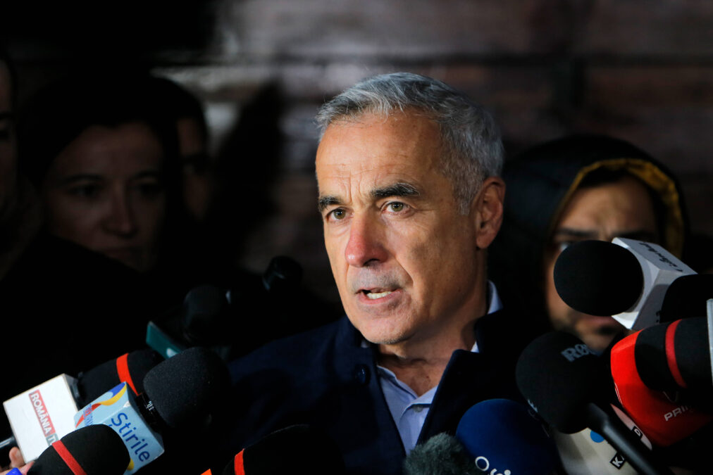 Călin Georgescu spricht vor einem dunkeln Hintergrund in Mikrofone.