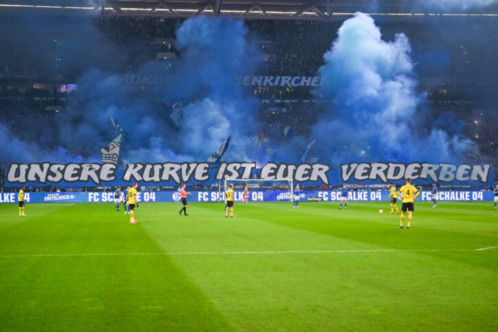 Schalke-Spiel in der Veltins-Arena. Am Spielfeldrand das Banner "Unsere Kurve ist euer Verderben"