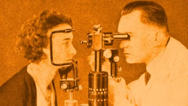 Black and white image of a young woman having her eyes examined by a doctor.