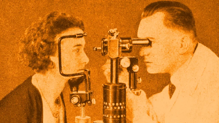 Black and white image of a young woman having her eyes examined by a doctor.