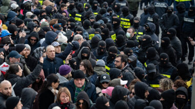 Menschen stehen maskierten Polizeiketten entgegen.