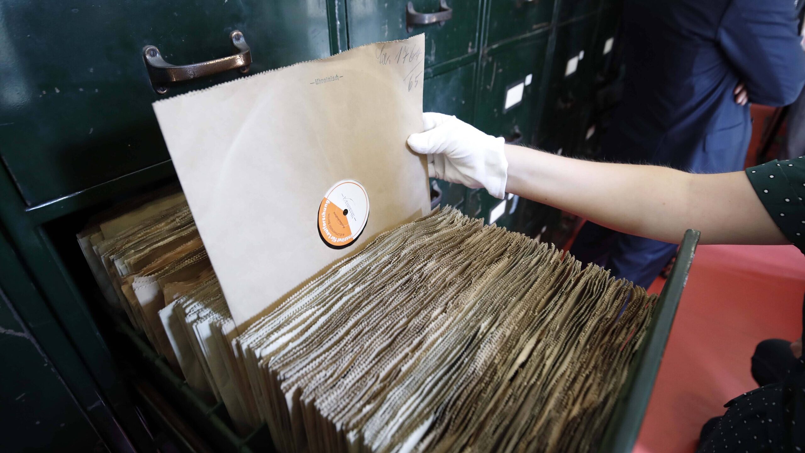 Hand mit Gummihandschuh zieht eine alte Schallplatte aus einem Archiv