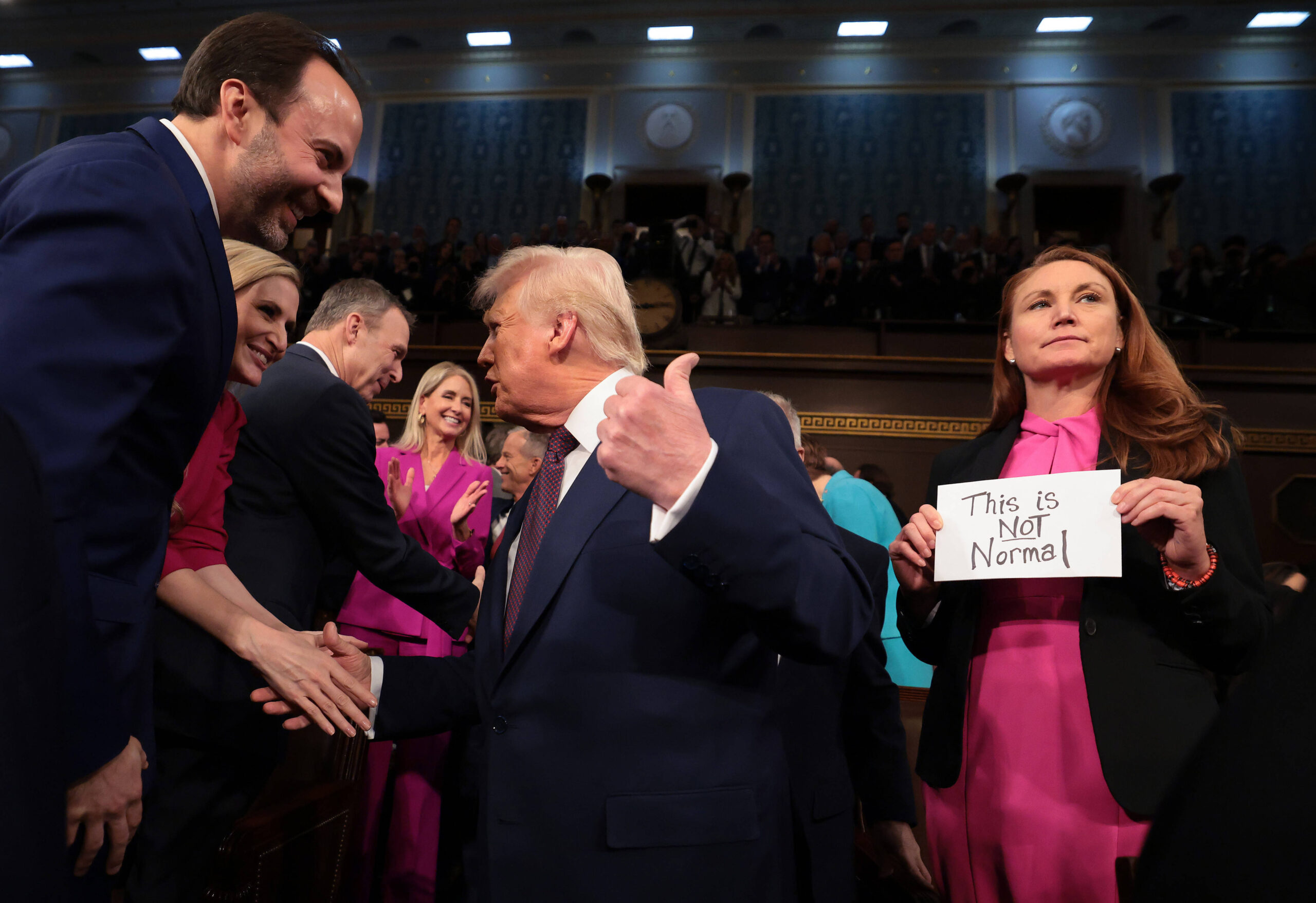 Trump schüttelt Hände im US-Congress, hinter ihm hält jemand ein Schild "This is not normal".